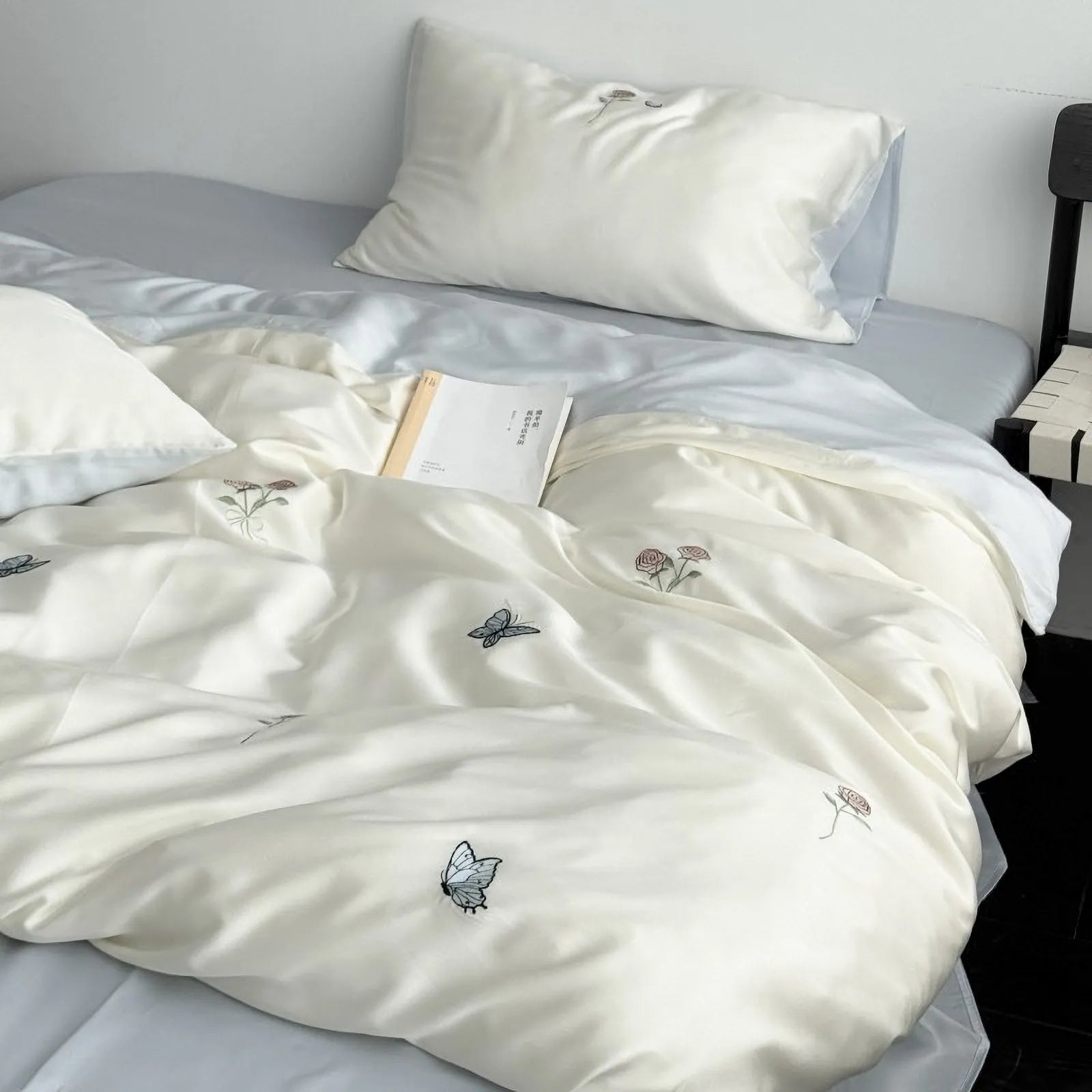 Full view of the Cream White embroidered butterfly and rose Tencel bedding set on a bed in a minimalist room.