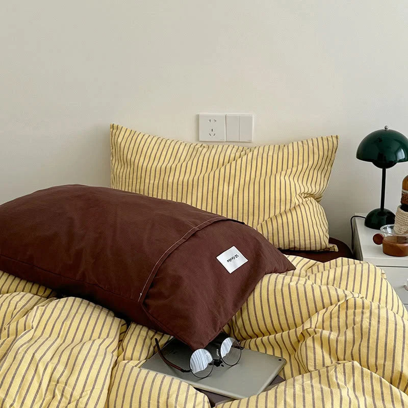 Close-up of the pillow arrangement, featuring a solid brown pillowcase in front of a Yellow & Brown striped one - RoomDen.