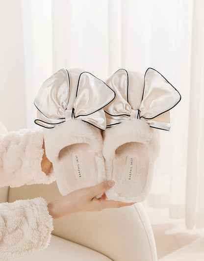 Close up of oversized satin bows on cream plush slippers held in hands