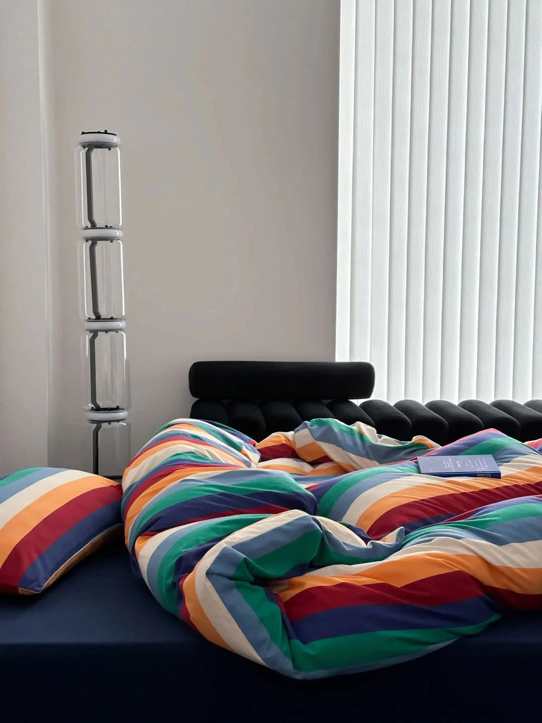The rainbow striped duvet cover in a bright, modern bedroom with a unique floor lamp and black headboard - RoomDen