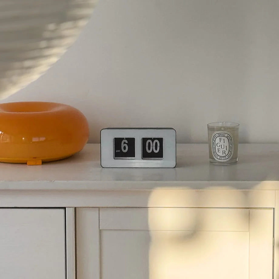 Black and white retro flip clock on a white dresser next to a candle and an orange lamp. - RoomDen