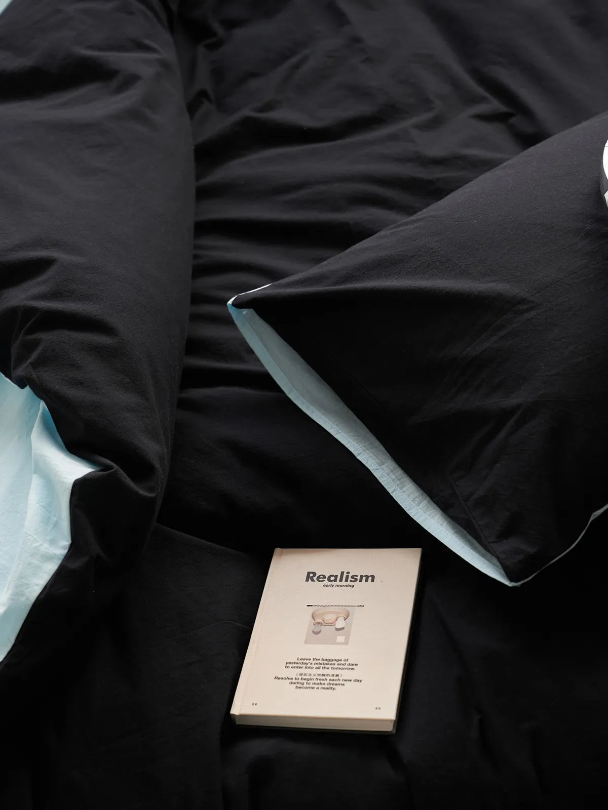 Top-down view of the Reversible Two-Tone Washed Cotton Bedding Set with a book resting on the black pillow, showing the cyan reverse side.