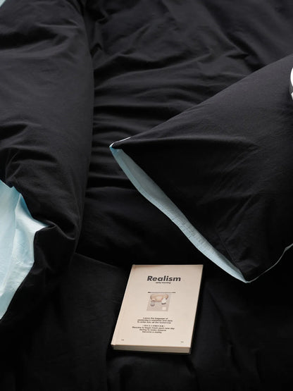 Top-down view of the Reversible Two-Tone Washed Cotton Bedding Set with a book resting on the black pillow, showing the cyan reverse side.