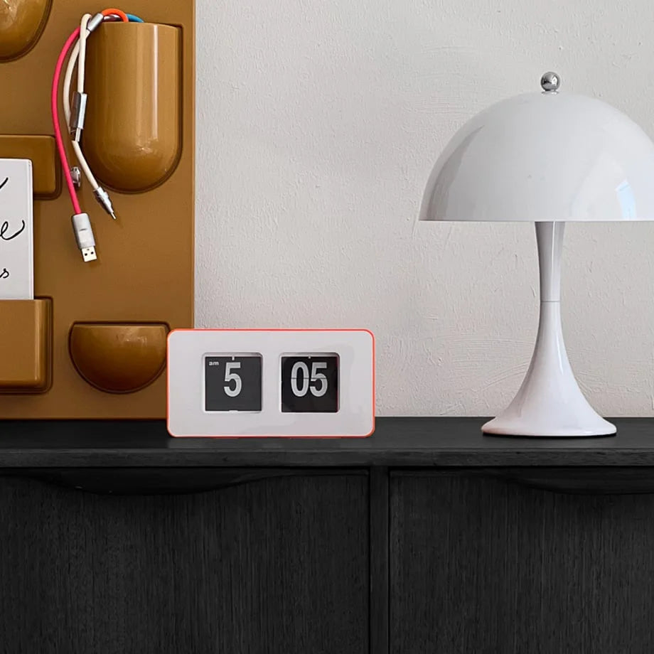 The orange and white minimalist flip clock styled on a desk next to a white lamp. - RoomDen