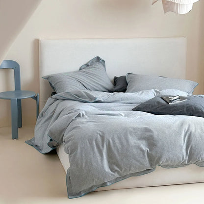 Angled shot of the Dark Grey & Blue Pinstripe Washed Cotton Bedding Set on a bed with a blue chair nearby.