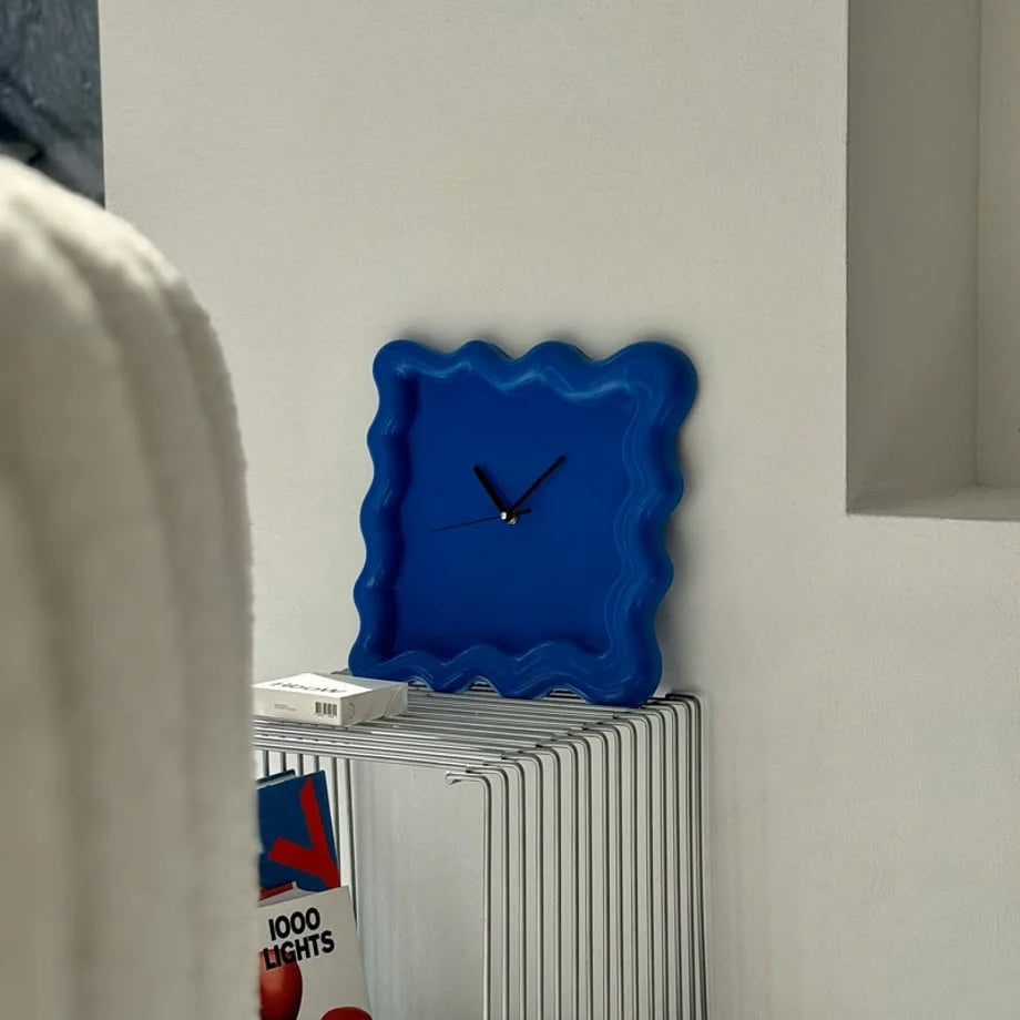 Lifestyle shot of the blue Wavy Squiggle Clock on a modern metal table in a bright, minimalist room. - RoomDen