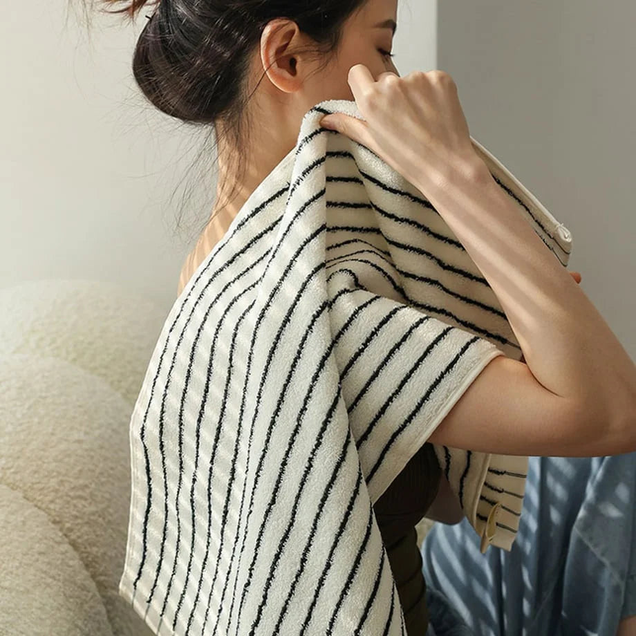 A woman gently drying her neck with the soft white and black striped face towel.