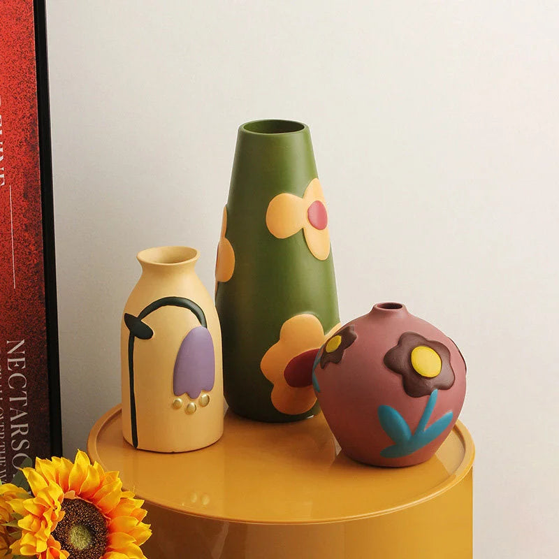 Close-up of three floral ceramic vases on a yellow table next to a book and a sunflower. - RoomDen