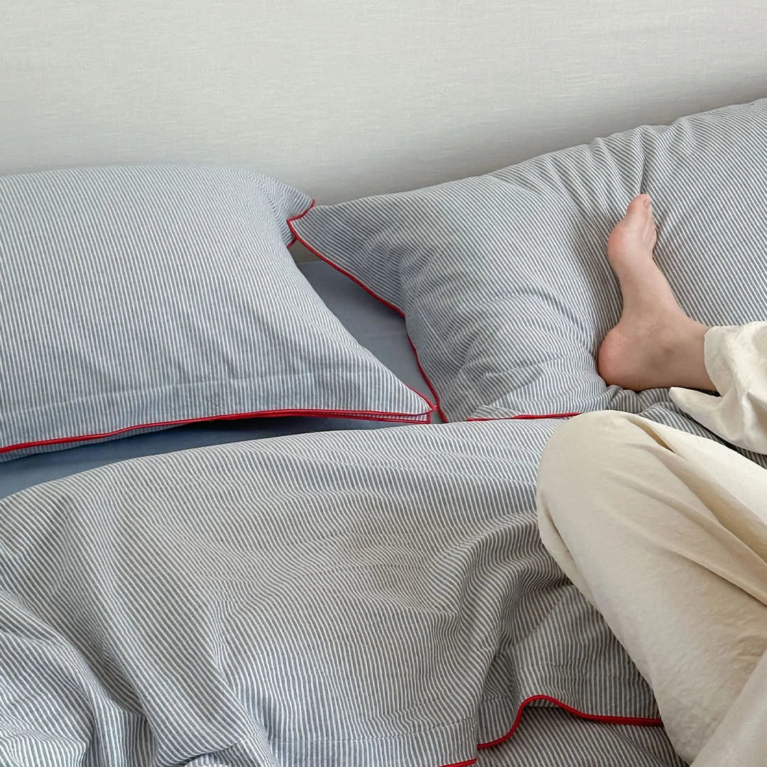 A person's foot resting on the cozy Light Grey & Red Pinstripe Washed Cotton Bedding Set.