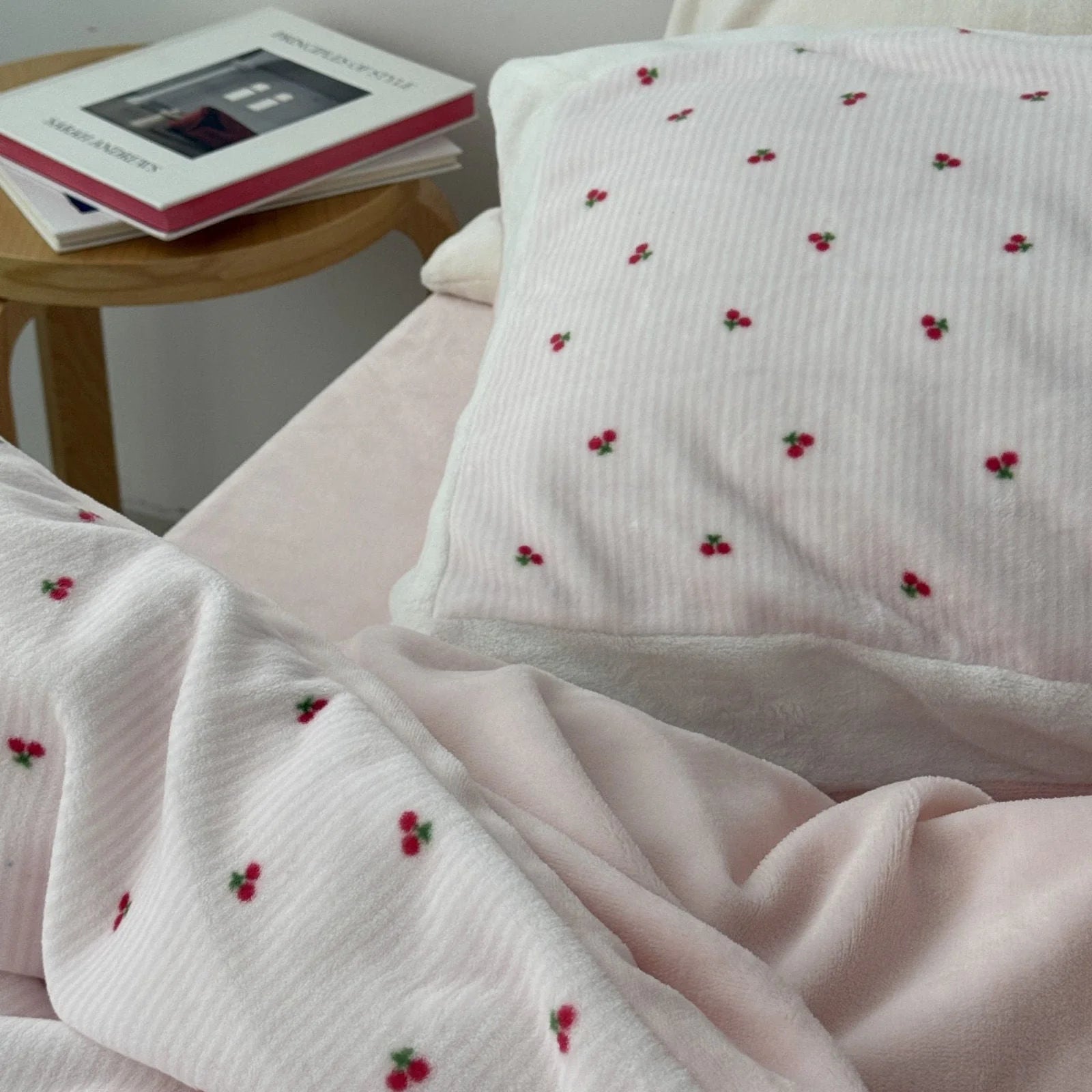 Close-up of the cherry print pillowcase, showing the soft texture next to a wooden side table with books. - RoomDen