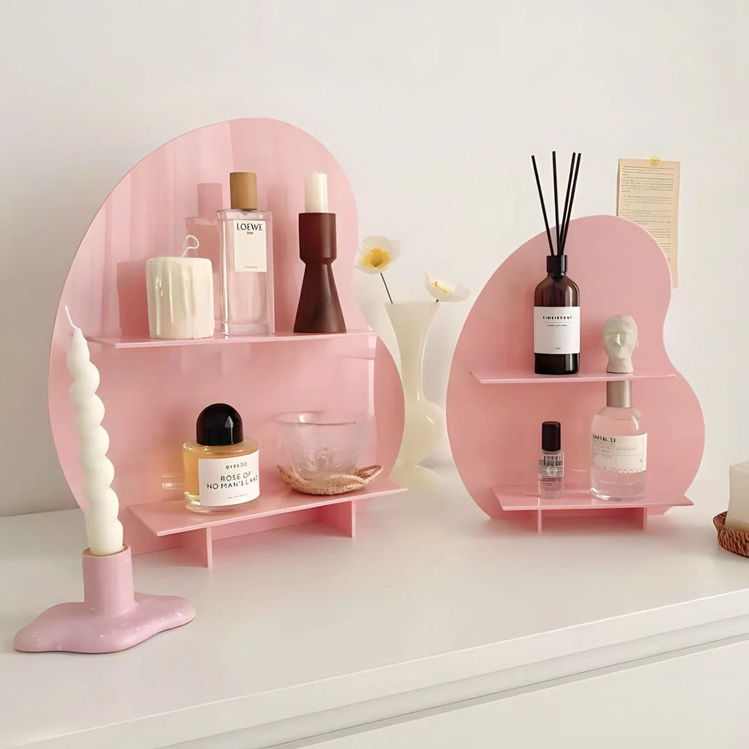A pink wavy acrylic desktop organizer displaying perfumes and a candle on a white desk. - RoomDen