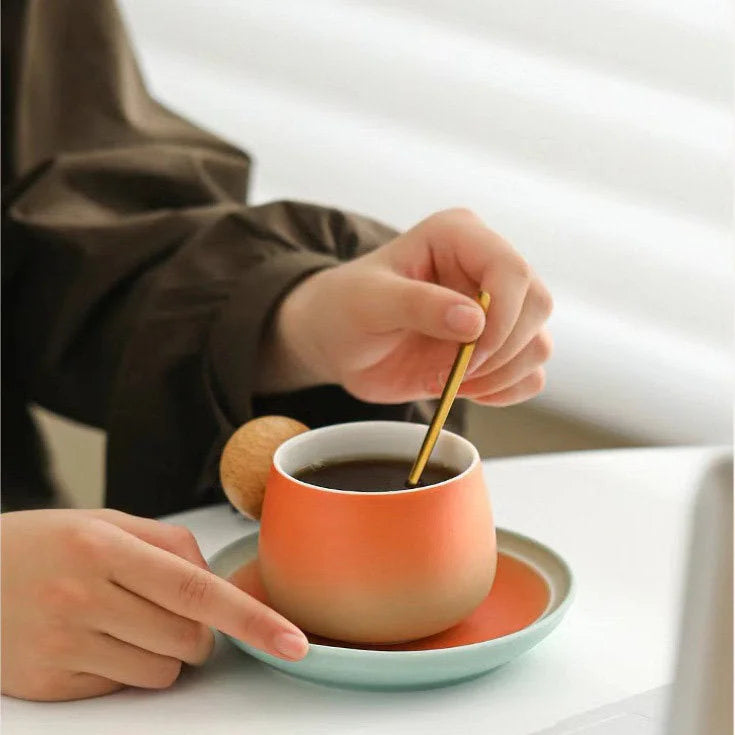 Close-up of a hand stirring coffee in the Sunset Orange gradient ceramic mug with a wooden handle. - RoomDen