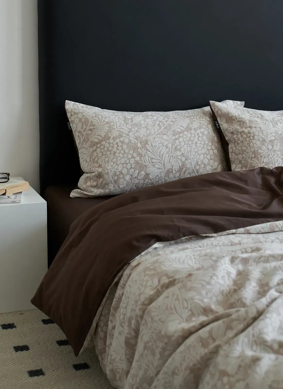 A focused view of the taupe brown pillowcases against a black headboard, part of the Jacquard Botanical Bedding Set - RoomDen.