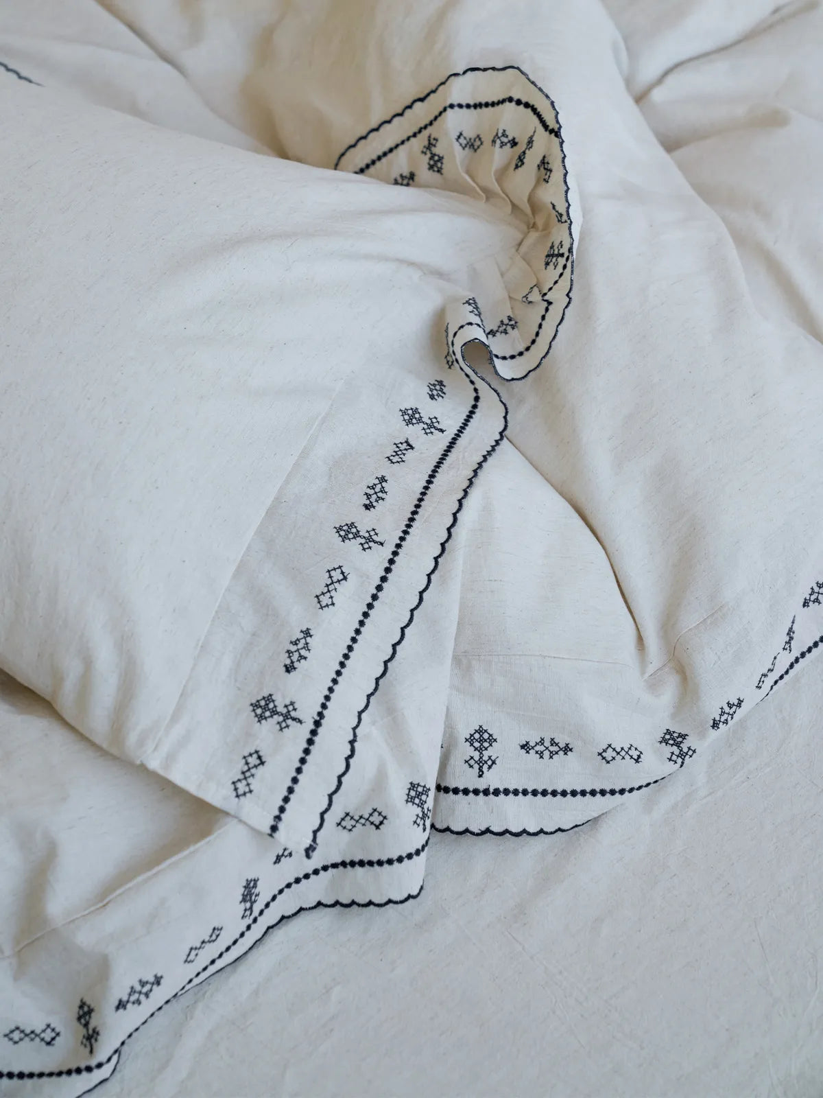 Close-up view of the overlapping embroidered ruffle edges of the linen duvet cover and pillowcase - RoomDen.