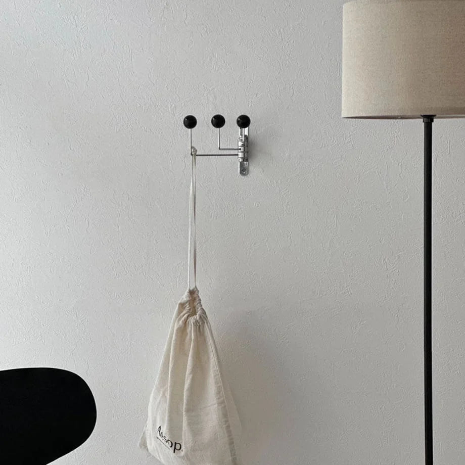 The black metal ball-end hook mounted in a minimalist room, holding a cream canvas bag - RoomDen.