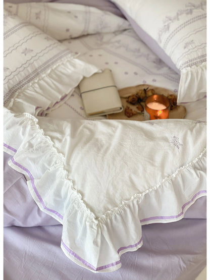 Detail of the ruffled pillowcase corner with lavender trim from the embroidered bedding set.