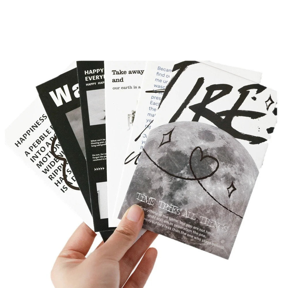 Hand holding a fan of five monochrome typographic and photographic cards from the wall collage kit - RoomDen.