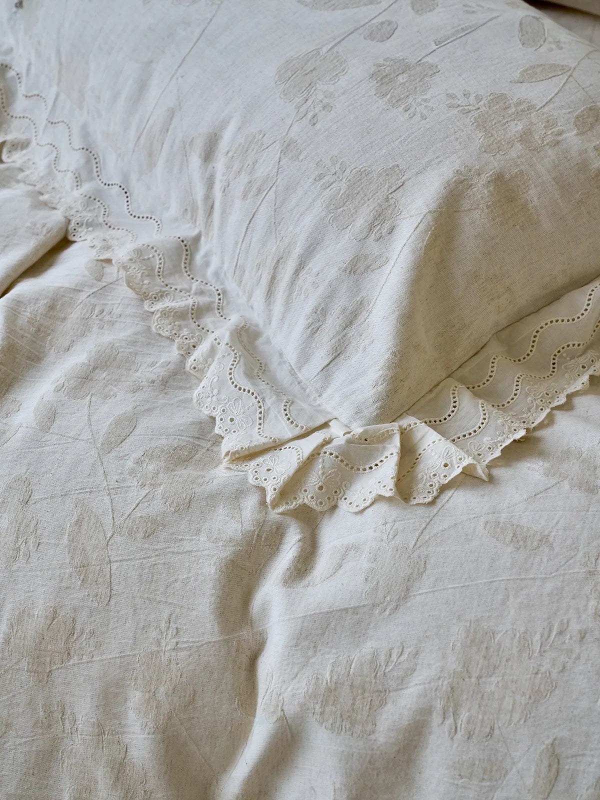 Detailed close-up of the eyelet lace ruffle trim on an Antique White linen pillowcase with a floral jacquard pattern - RoomDen