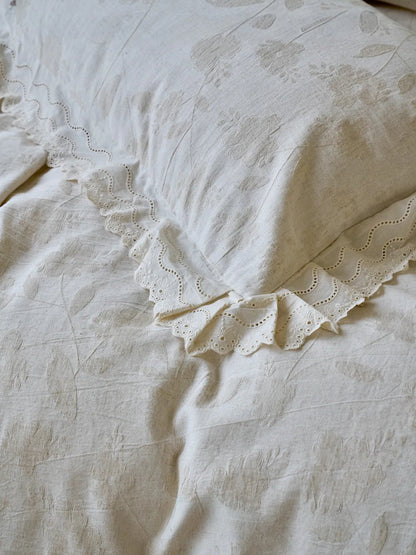 Detailed close-up of the eyelet lace ruffle trim on an Antique White linen pillowcase with a floral jacquard pattern - RoomDen