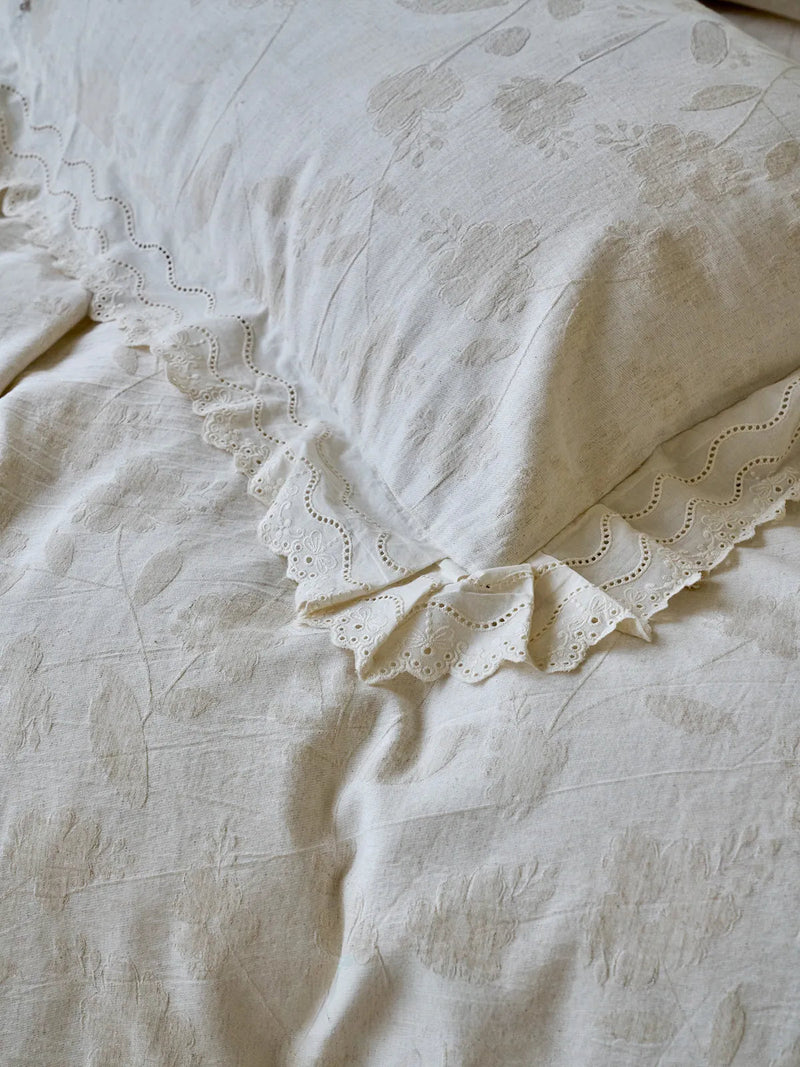 Detailed close-up of eyelet lace ruffle trim on an antique white floral jacquard pillowcase — RoomDen