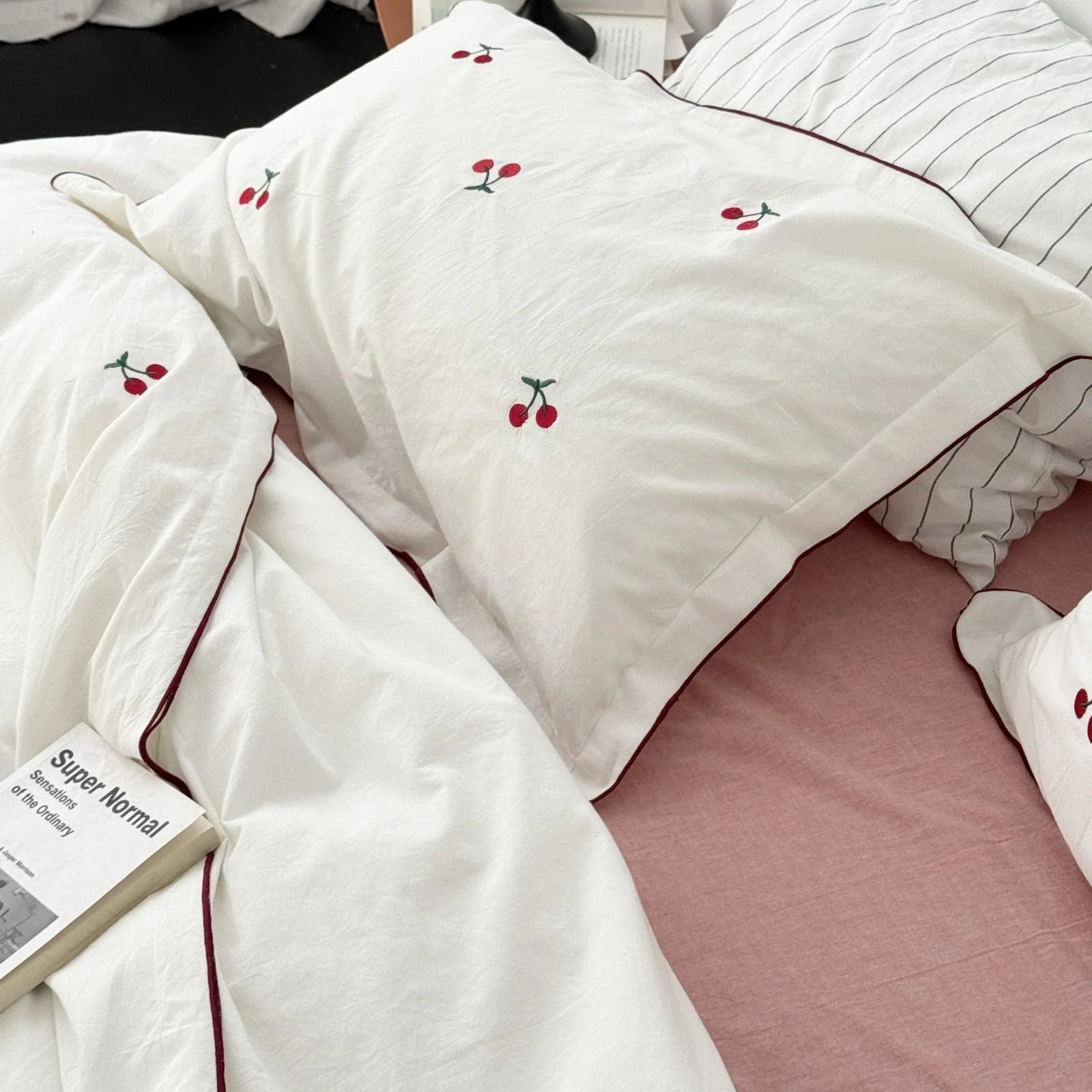 Close-up of the pure white pillowcase with embroidered cherries, next to a 'Super Normal' book.