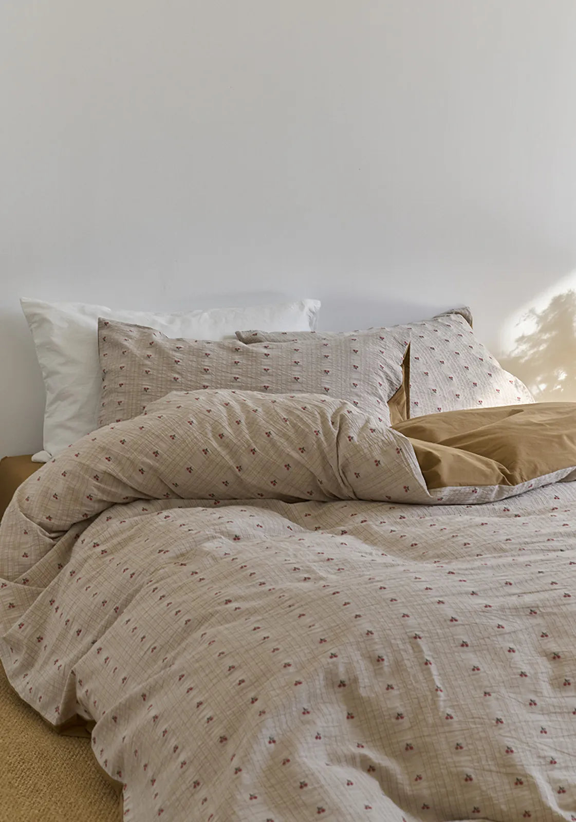 The Textured Ditsy Cherry Washed Cotton Bedding Set styled on a bed with soft morning light hitting the pillows - RoomDen.