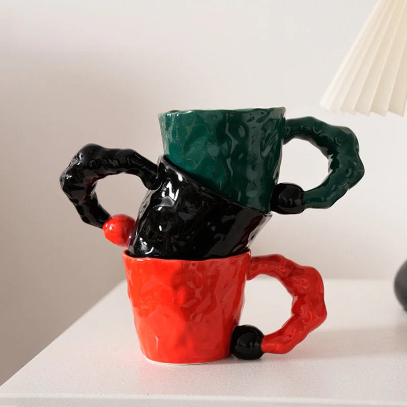 A stack of three artistic ceramic mugs in green, black, and red on a white desk - RoomDen.