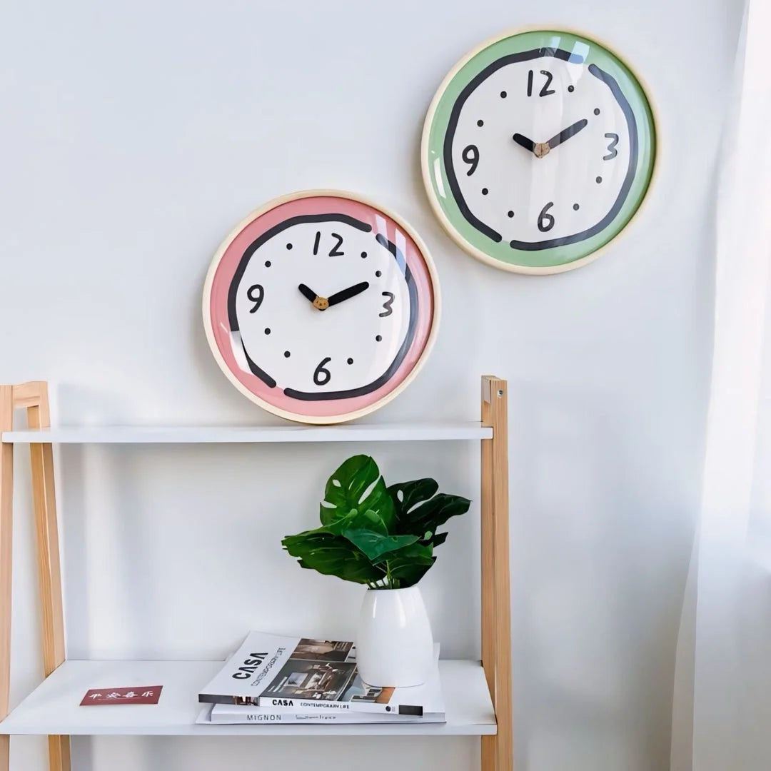 Pink and green Doodle Wall Clocks displayed on a white shelf with a plant - RoomDen.
