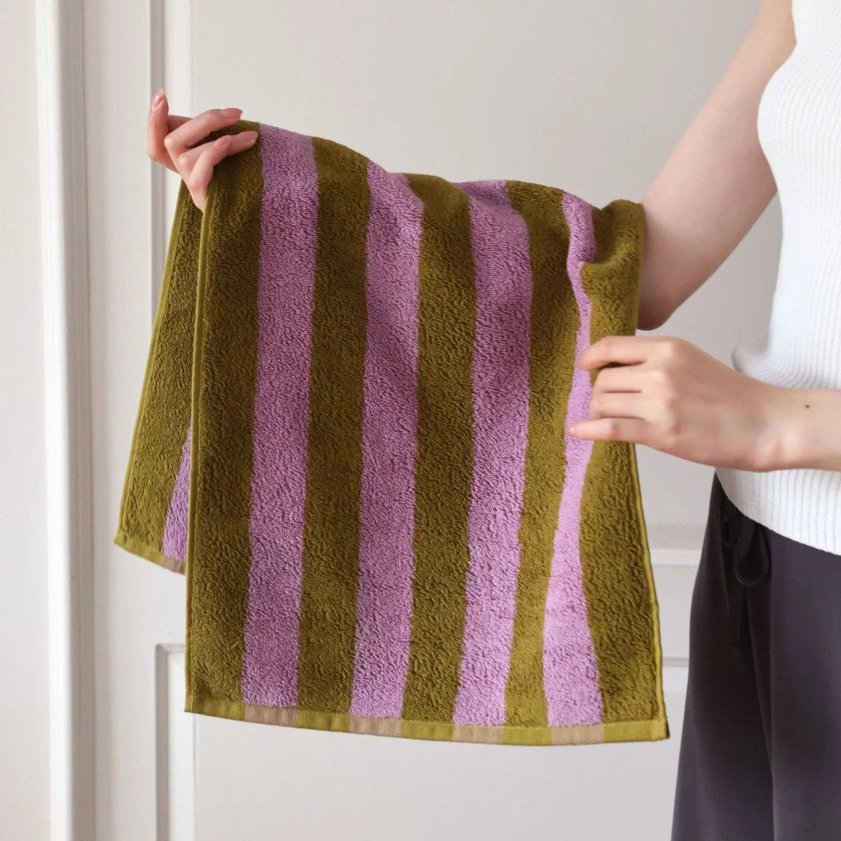 Close-up of hands holding the textured green and purple striped cotton face towel, showing the soft terry cloth. - RoomDen