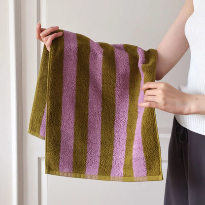 Close-up of hands holding the textured green and purple striped cotton face towel, showing the soft terry cloth. - RoomDen