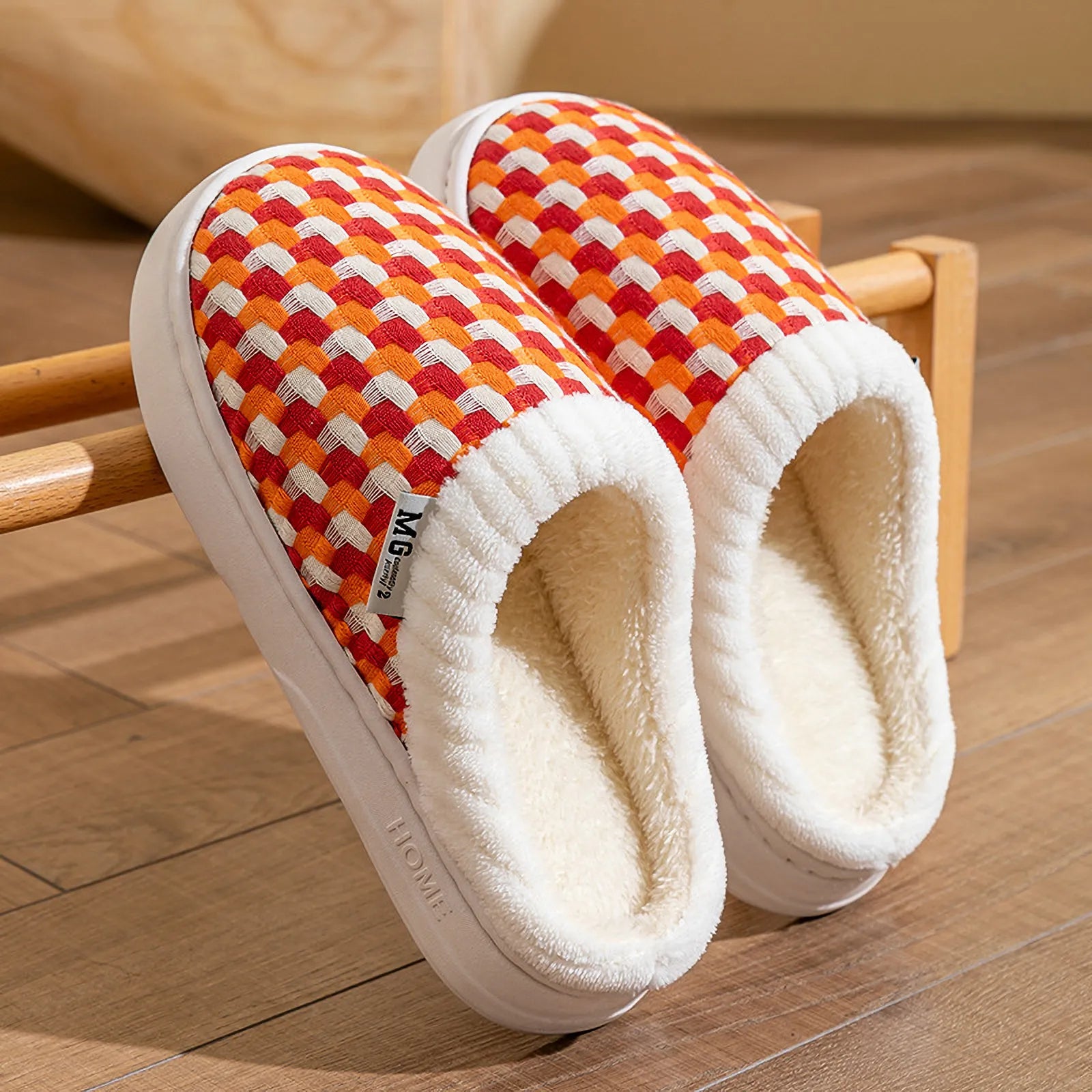 Pair of orange woven plush slippers resting on wooden rack