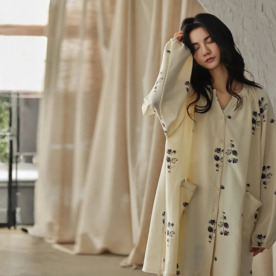 Model with eyes closed, relaxing in the oversized botanical print pajama top, standing by a window with cream curtains - RoomDen