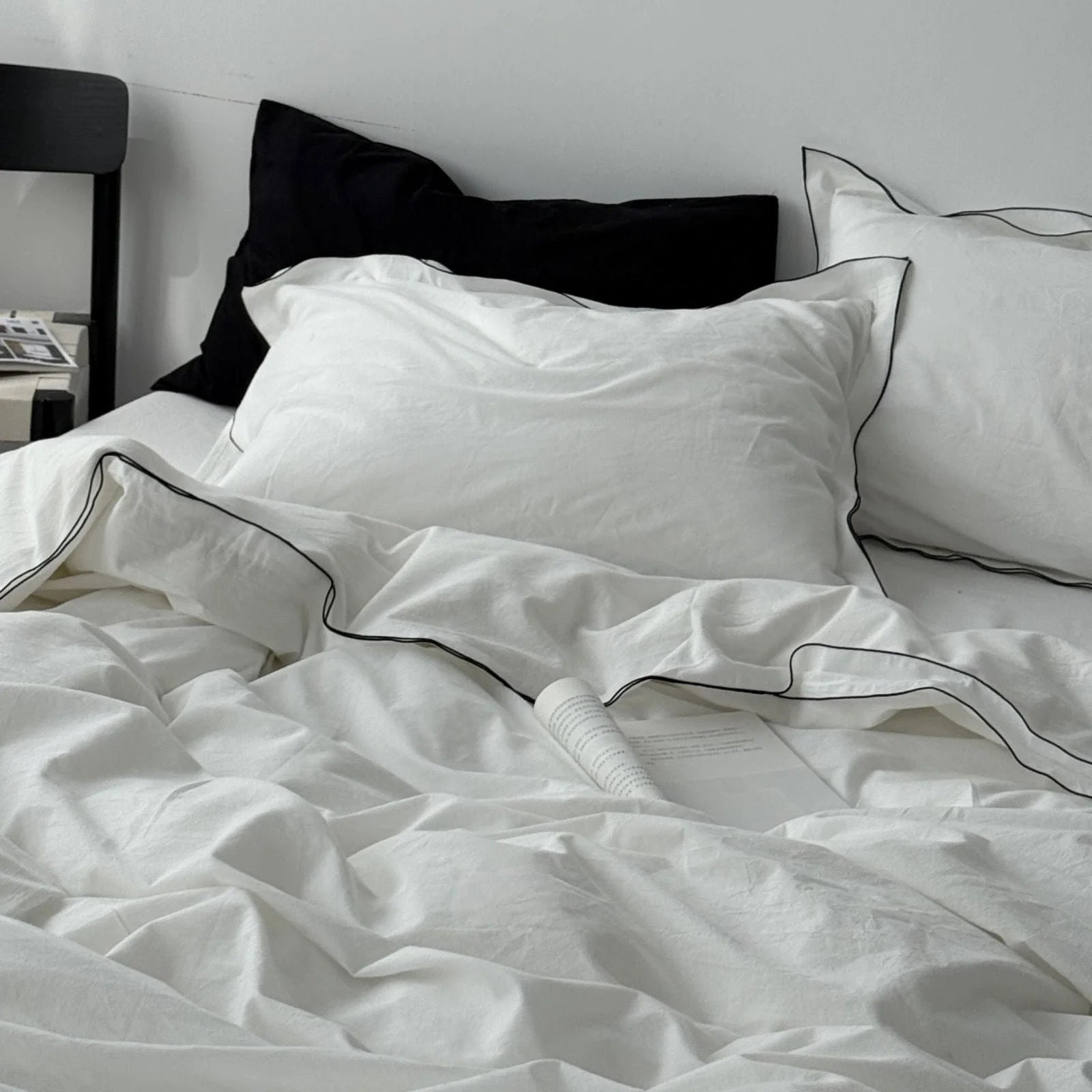 A cozy, unmade bed with a white washed cotton duvet cover and pillows, both featuring a delicate black trim. - RoomDen
