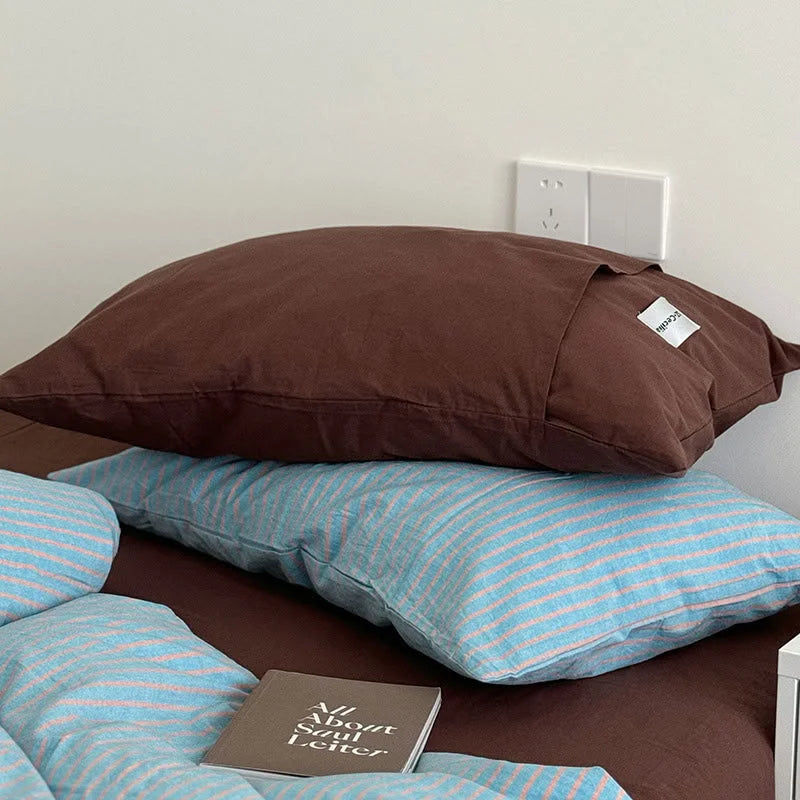 Detail shot focusing on the solid brown pillowcase resting on the Blue & Brown striped duvet cover - RoomDen.