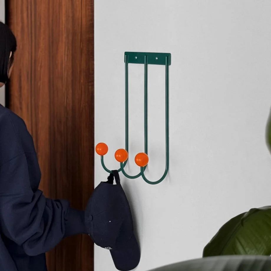 The Green & Orange Metal Wall Hooks installed next to a wooden door, holding a navy blue baseball cap. - RoomDen