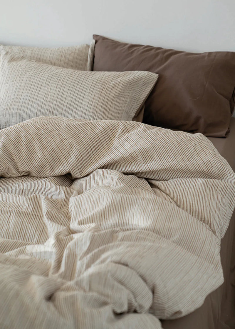 Detailed shot of the soft wrinkled texture of the Latte Brown washed cotton bedding, the warm tone muting shadow. — RoomDen