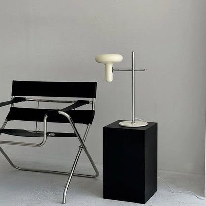 The Cream Sculptural Accent Lamp displayed on a black pedestal next to a modern chair - RoomDen.