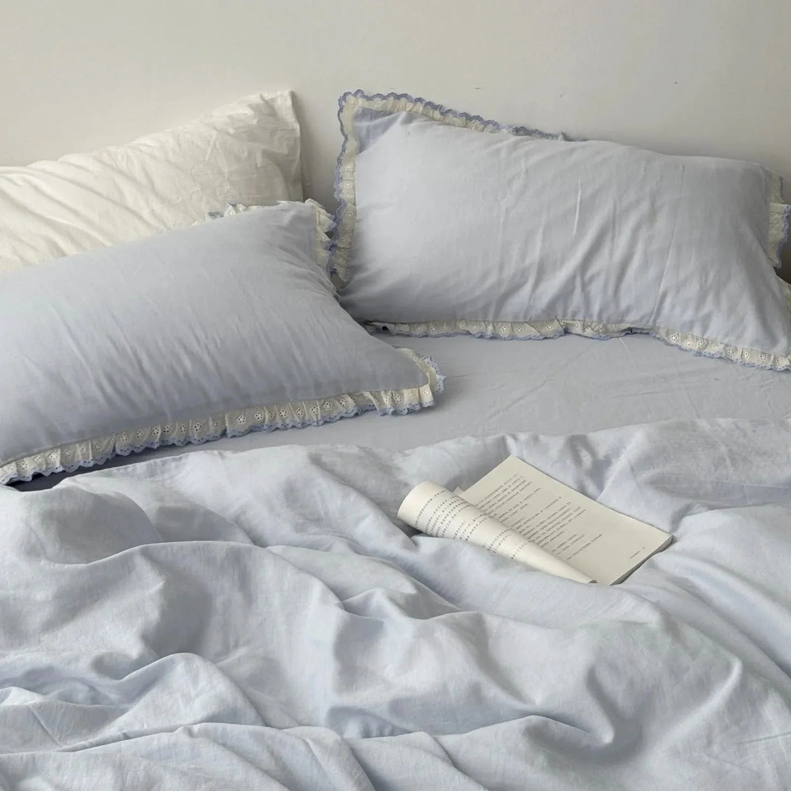 Sky blue lace ruffle bedding set with an open book resting on the duvet cover, creating a peaceful, academic vibe.