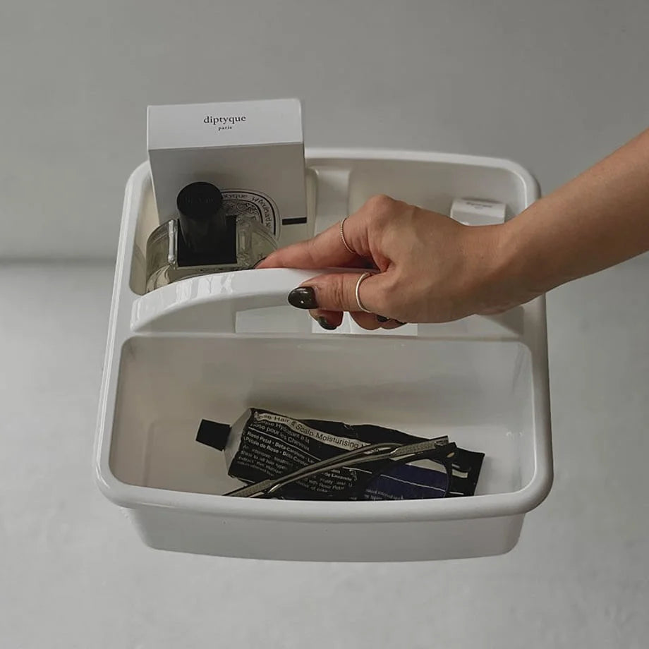 A hand holding the white organizer caddy, filled with Diptyque products and skincare tubes. - RoomDen