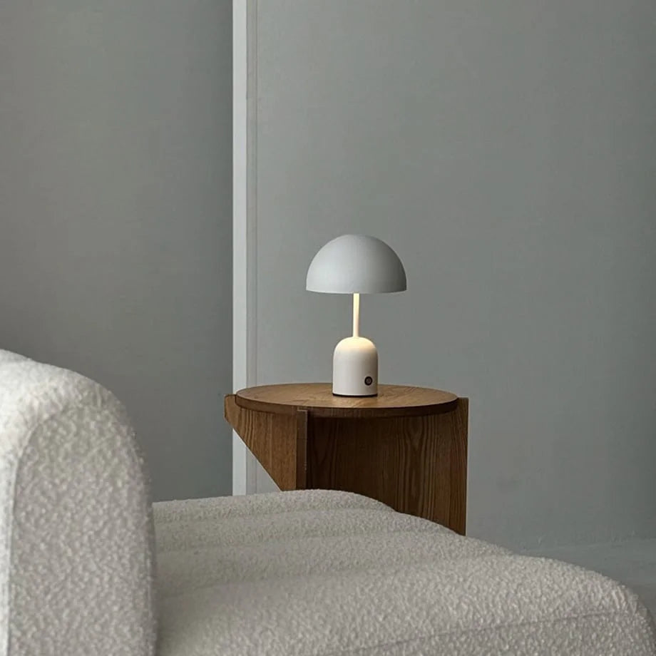 Off-White mushroom lamp on a wooden side table next to a cozy bouclé armchair - RoomDen