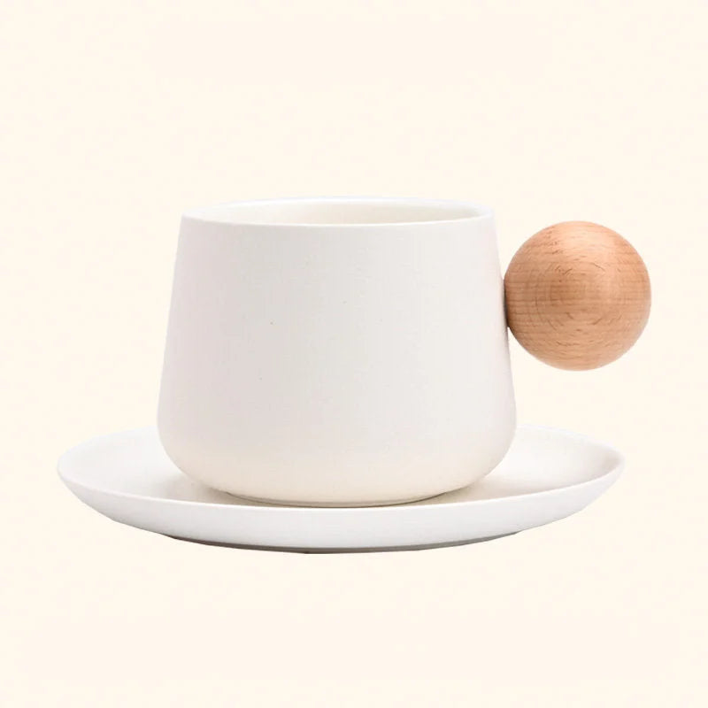 A studio shot of the Creamy White Frosted Ceramic Mug and Saucer Set with a wooden ball handle, showing a different angle. - RoomDen