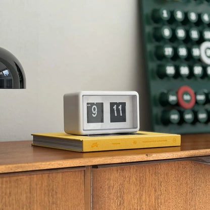 Minimalist retro flip clock in white on a wooden desk with a yellow book. - RoomDen