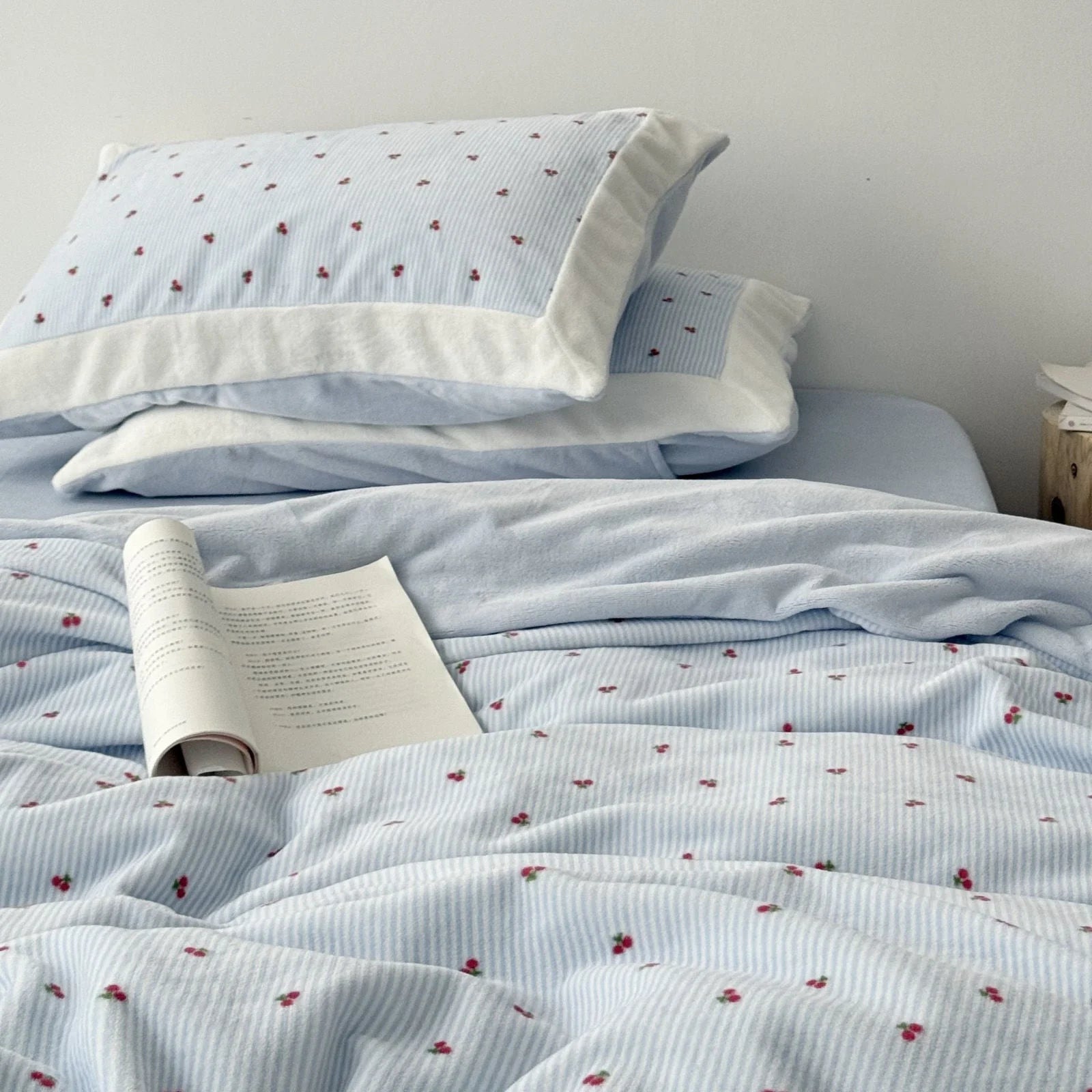 Close-up of a plush light blue cherry pinstripe flannel fleece bedding set with an open book resting on the duvet cover - RoomDen.