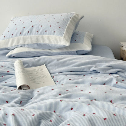 Close-up of a plush light blue cherry pinstripe flannel fleece bedding set with an open book resting on the duvet cover - RoomDen.