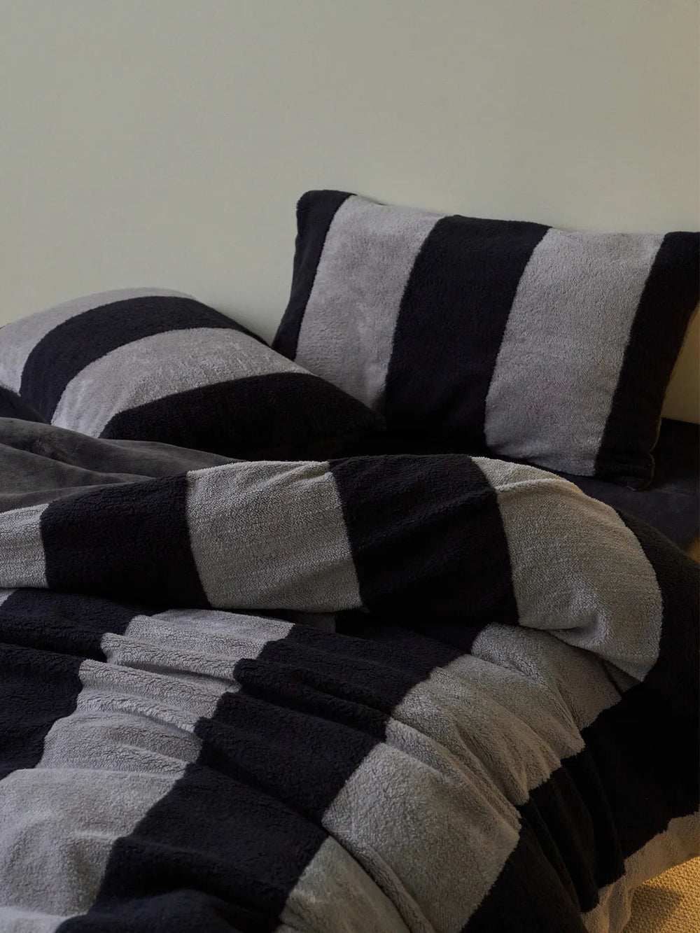 Close-up of the plush black and grey striped flannel fleece bedding set on a bed. - RoomDen
