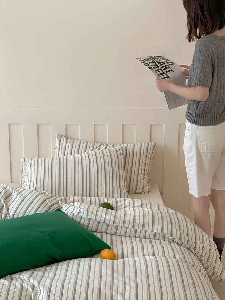 A person standing next to the bed made with the Grey Striped Washed Cotton Bedding Set. - RoomDen