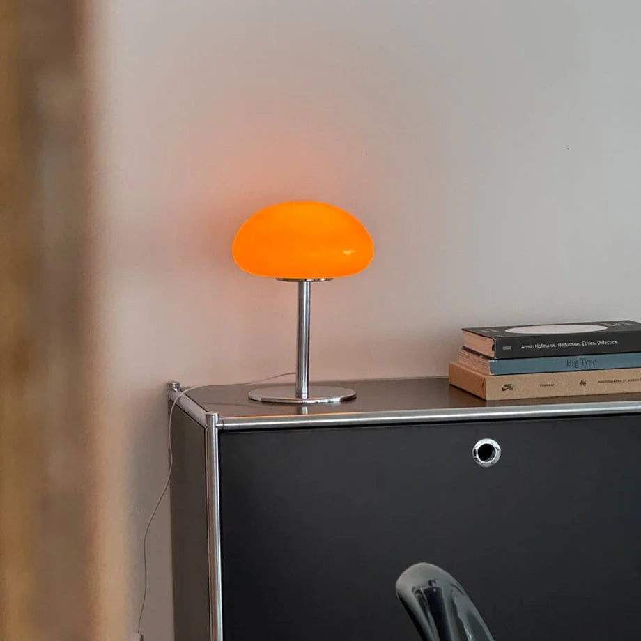 Angled view of the glowing orange mushroom lamp on a black metal console table - RoomDen.