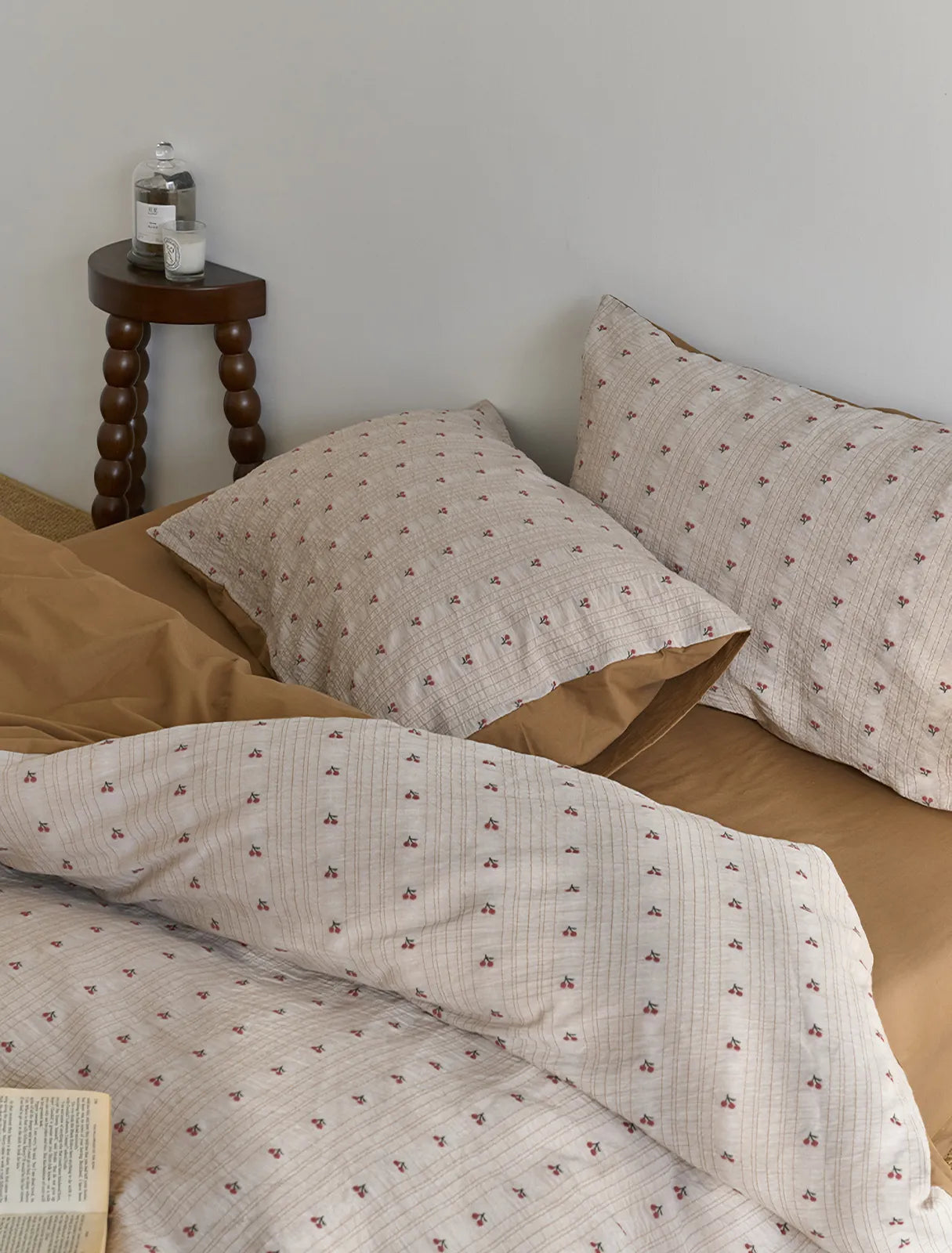 A close-up view of the corner of the bed showing the Ditsy Cherry pillow and duvet cover with a vintage-style nightstand - RoomDen.