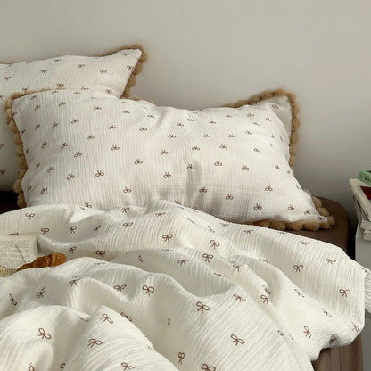 A clear shot of the two pom-pom trimmed pillows and the bow print duvet cover on a neatly made bed. - RoomDen