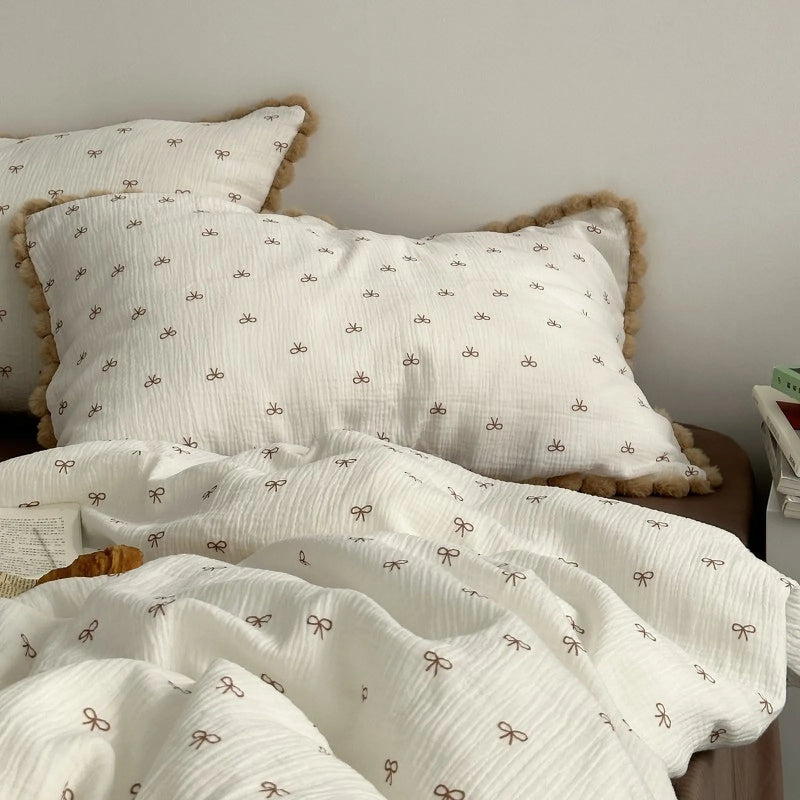 Two pom-pom trimmed pillows and the bow print duvet cover on a neatly made bed — RoomDen